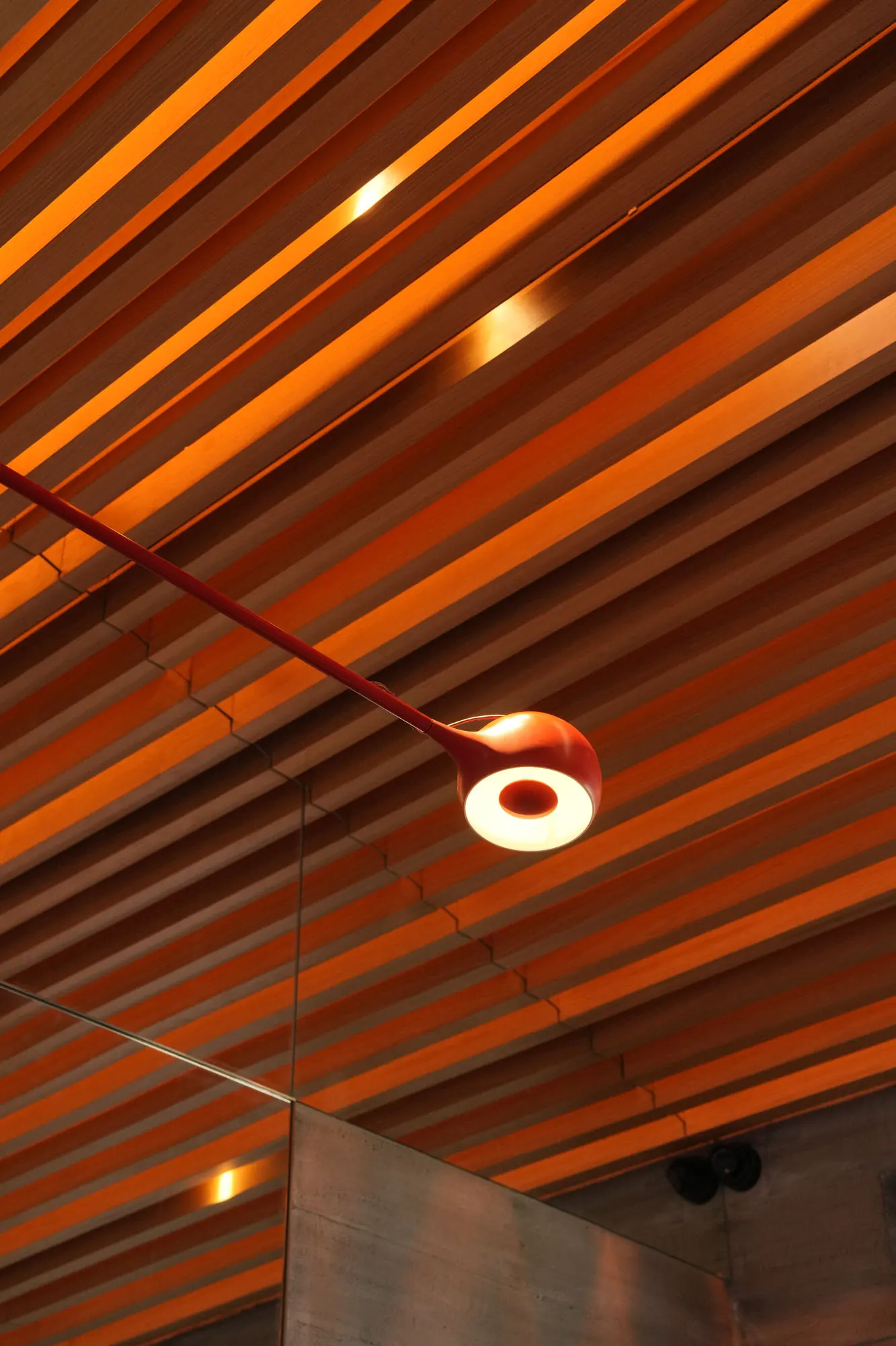 Close view of a red lamp head glowing beneath the warm timber slats