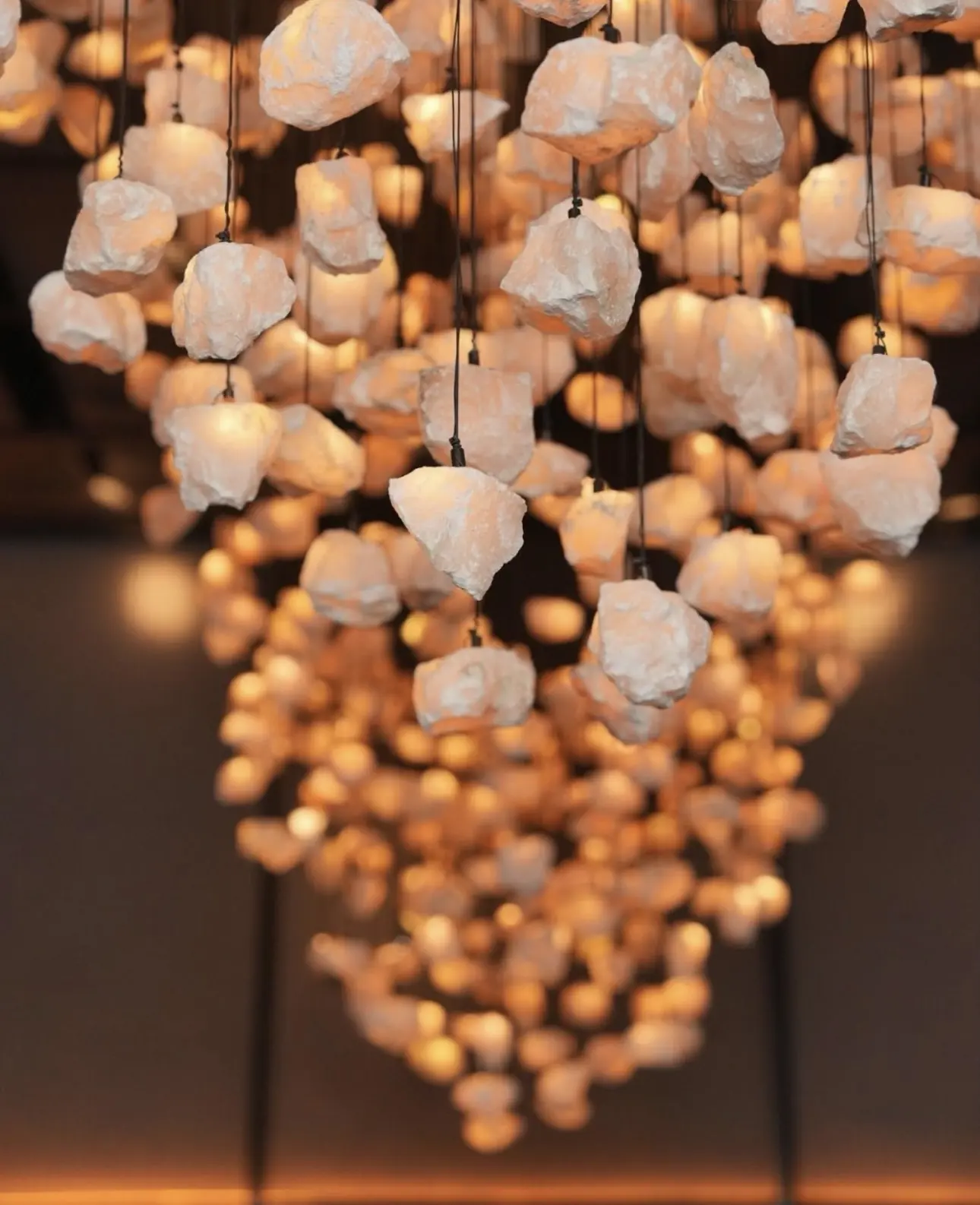 Close-up of hand-crafted pink onyx pieces, each lit and hung on its own cable